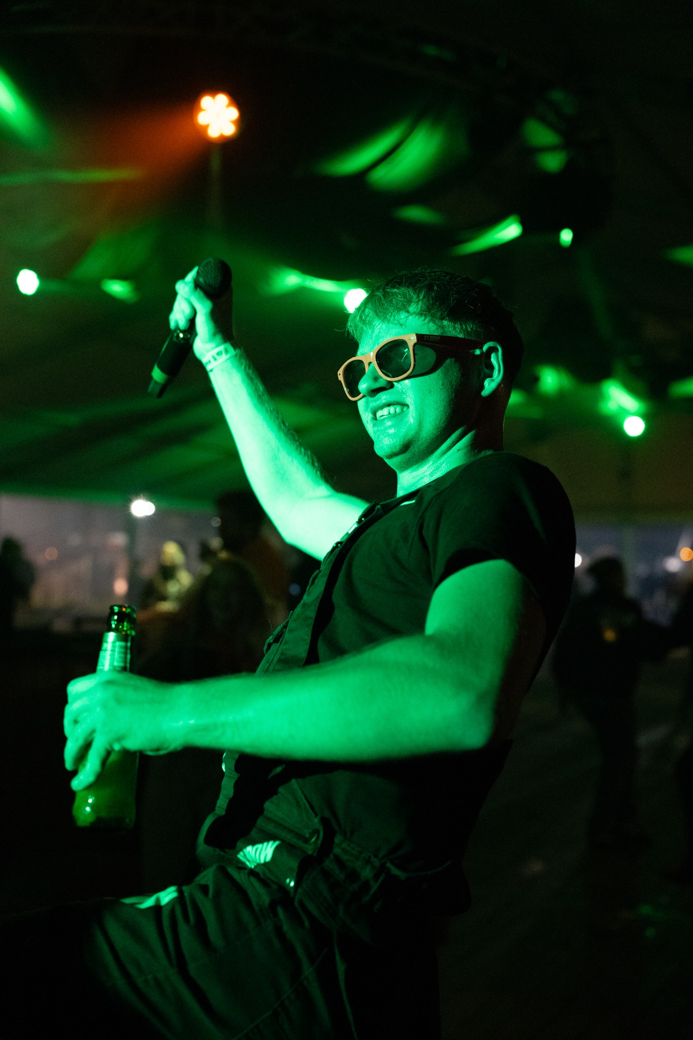 Performer with orange glasses and a beer bottle in green light