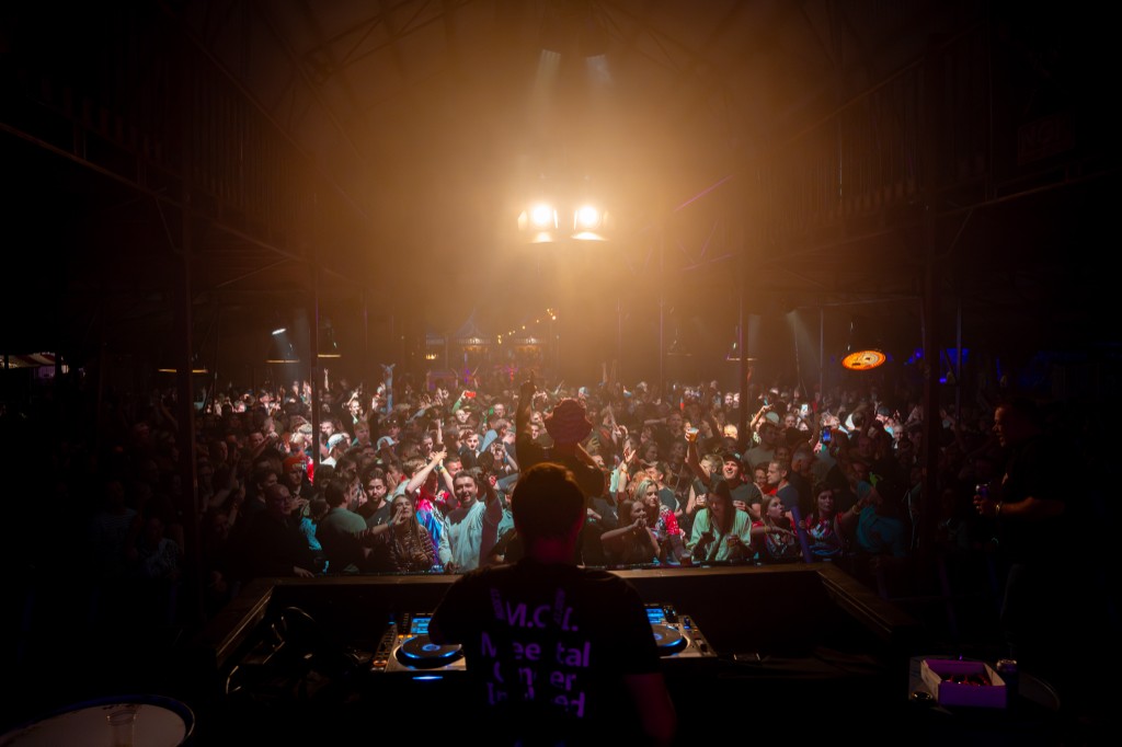 DJ from behind with arms raised toward the crowd in the party tent