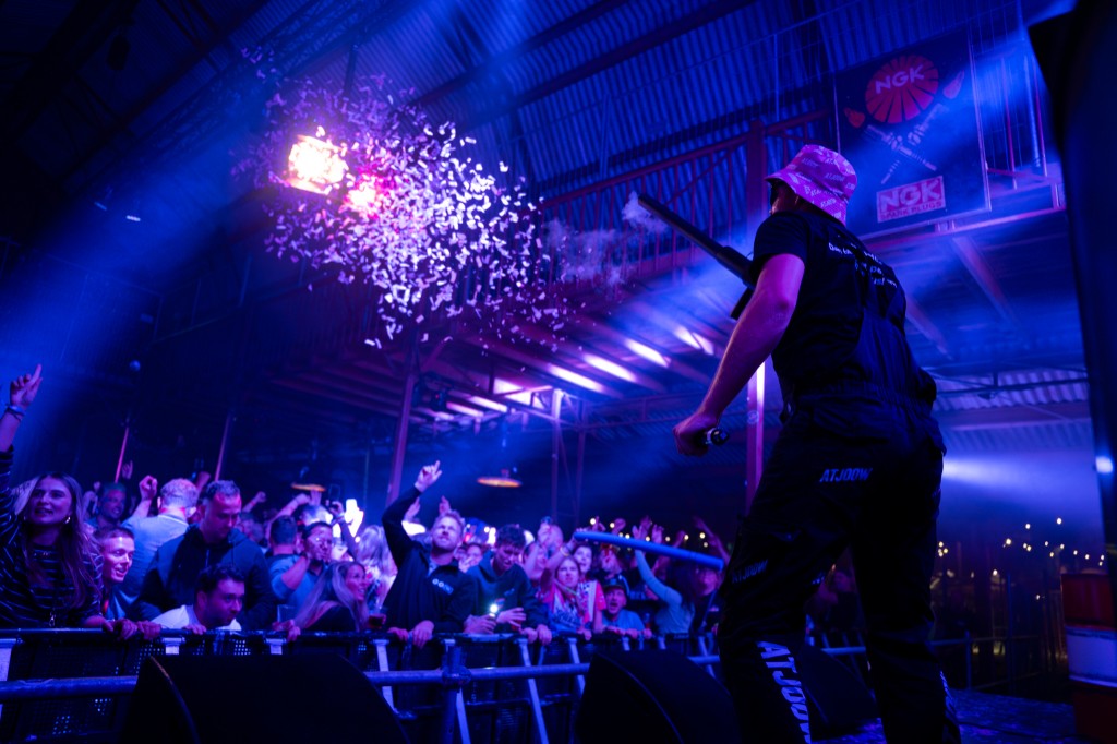 Artist firing a confetti cannon toward the crowd in a pink ATJOOW hat