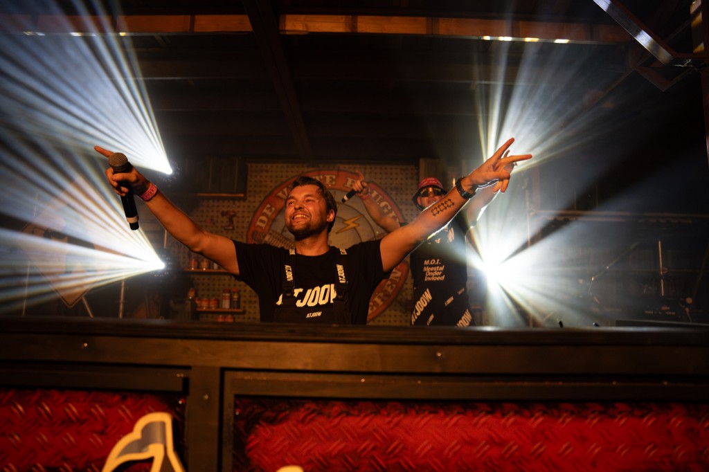 Both performers on stage with arms outstretched under white spotlights