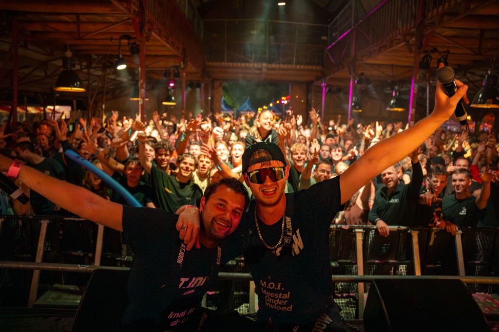 Both Atjoow performers smiling with microphones raised in front of the packed crowd