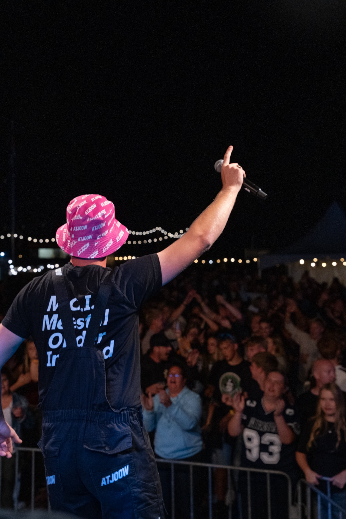 Performer from behind pointing toward the crowd in a pink ATJOOW hat