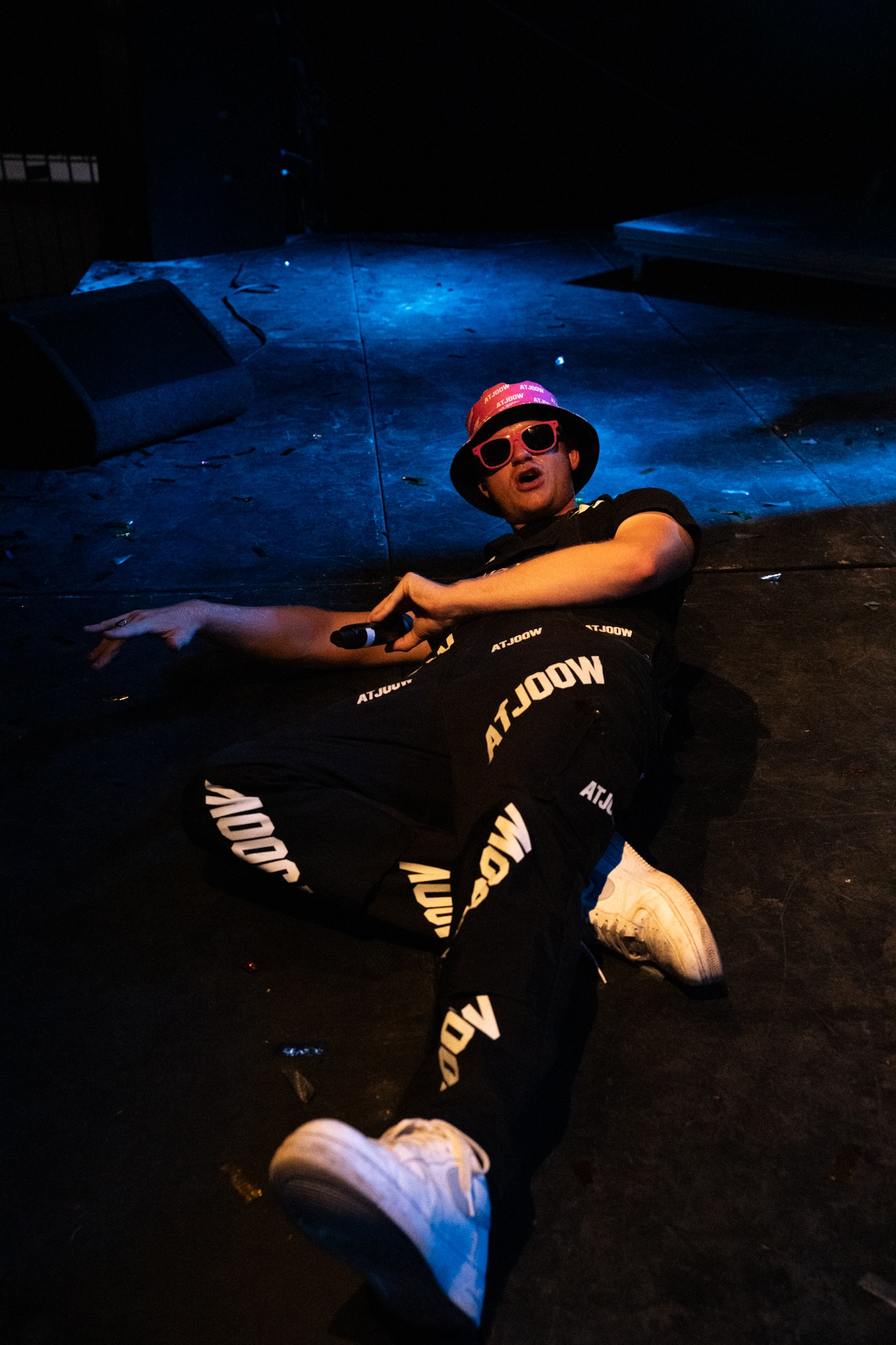 Performer reclining on the stage floor in a pink ATJOOW hat