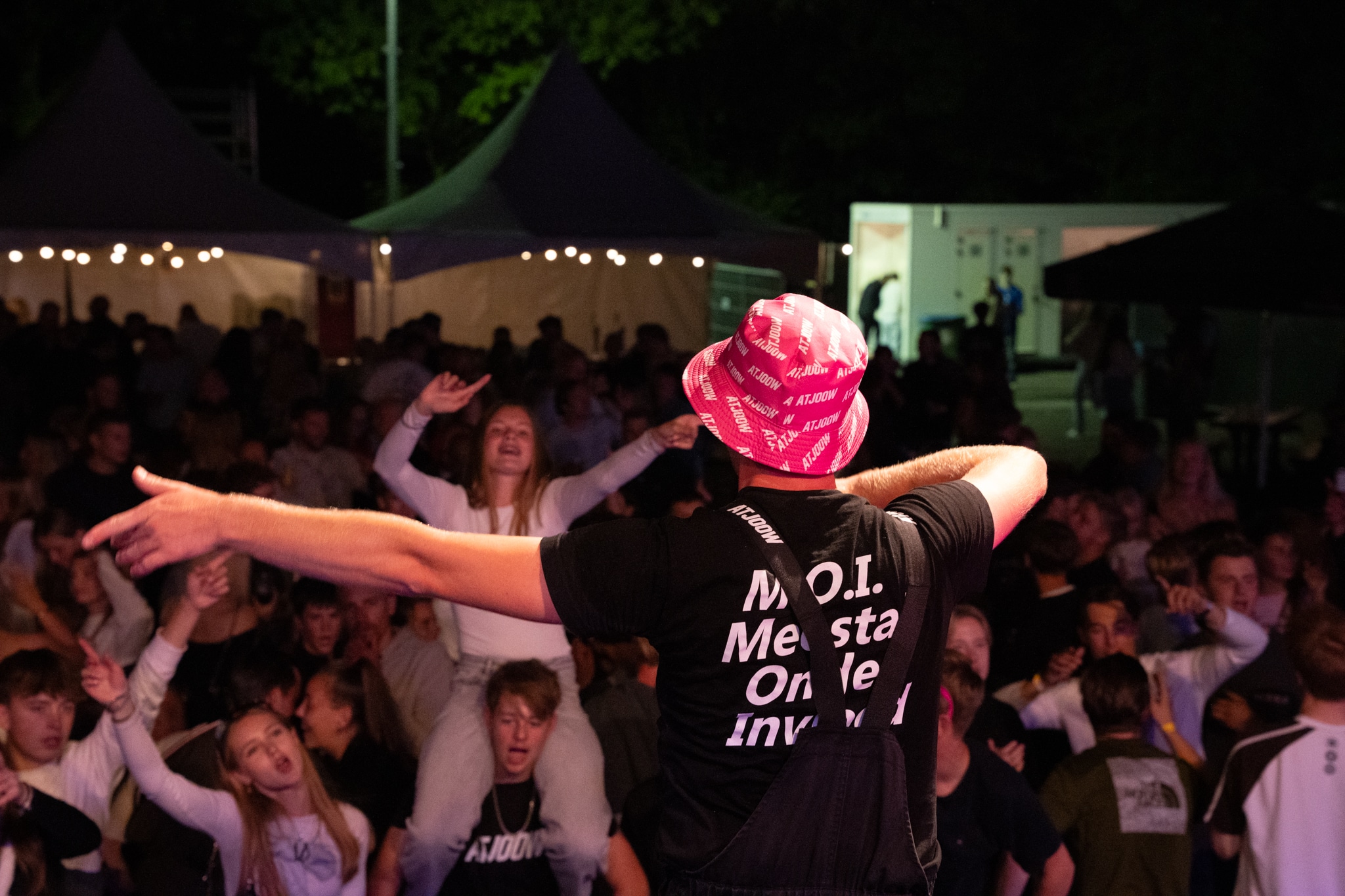 Artist from behind facing a packed outdoor crowd in a pink ATJOOW hat