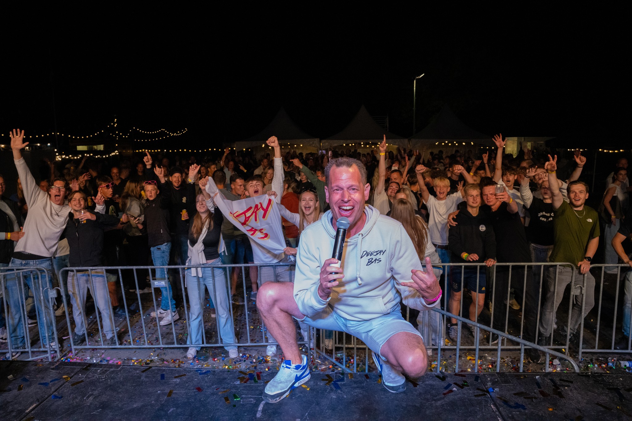 Deejay Bas crouched on stage cheering toward the camera with the crowd behind