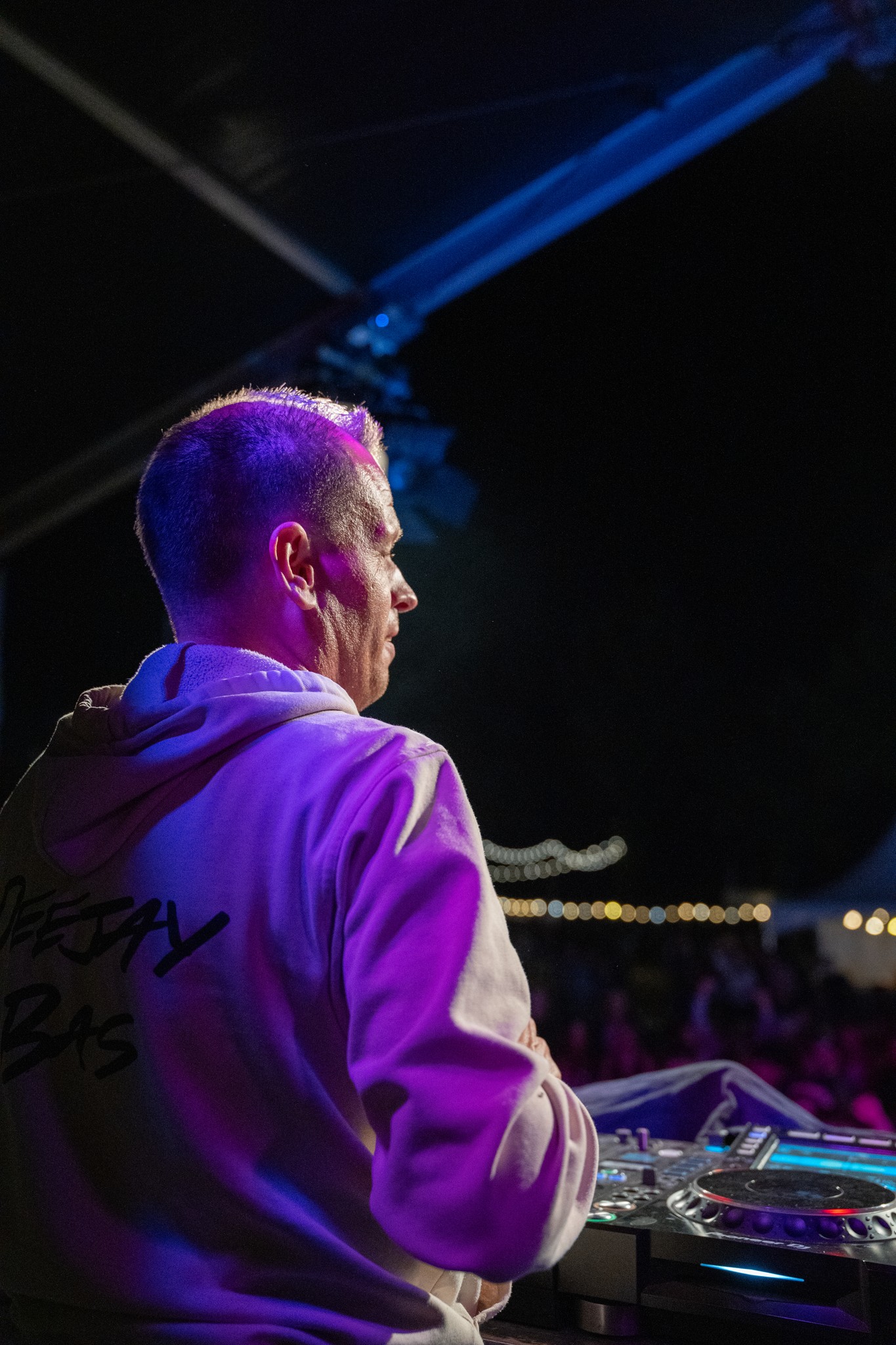 Deejay Bas from behind at the DJ controller under magenta stage light