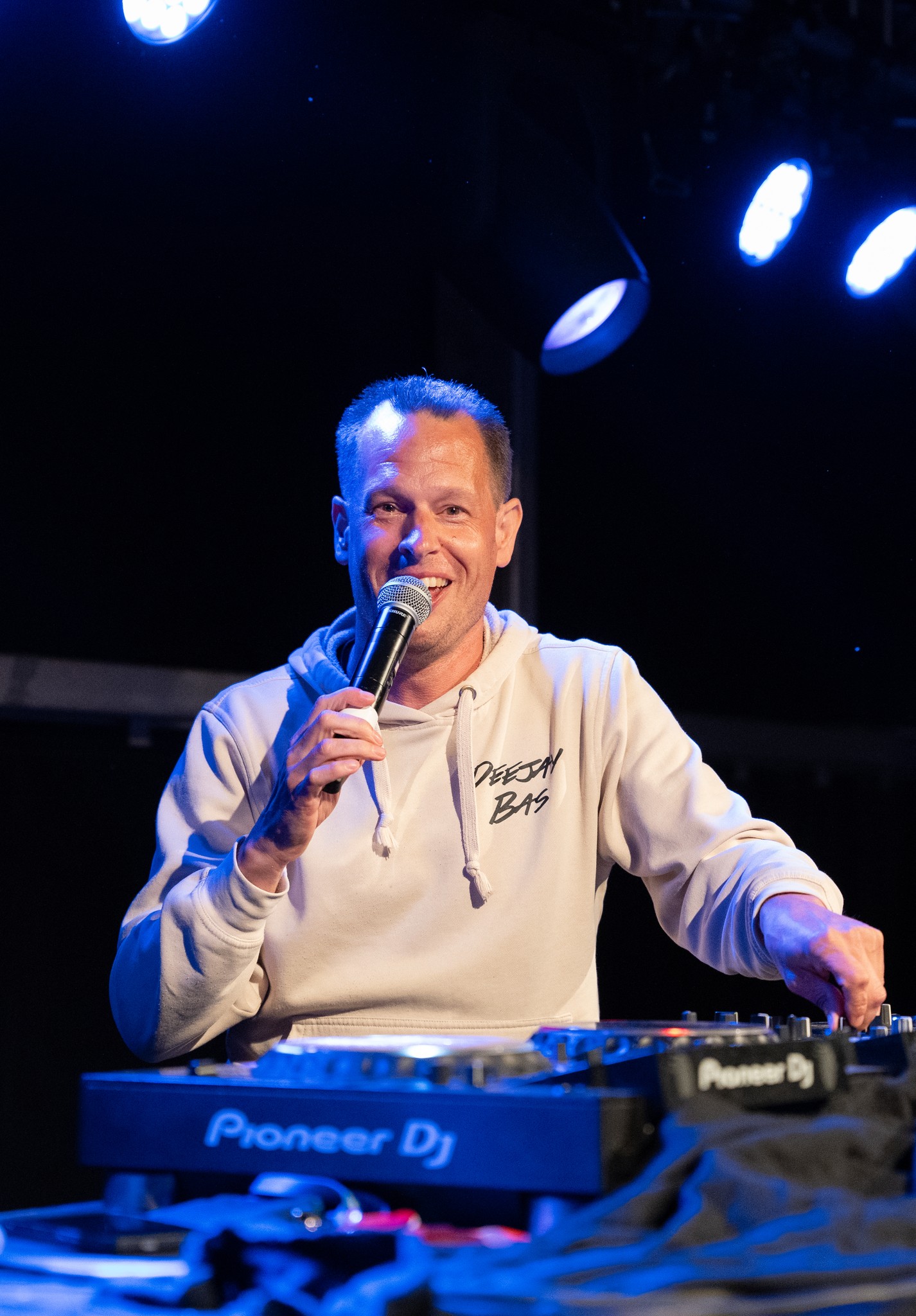 Deejay Bas smiling at the Pioneer mixer with microphone in hand